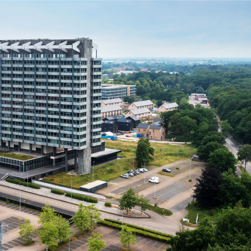 Luchtfoto van het VB-terrein in Eindhoven met een markant hoogbouwgebouw, omliggende bebouwing, groenvoorzieningen en de locatie waar de ontwikkeling van nieuwe appartementen plaatsvindt.