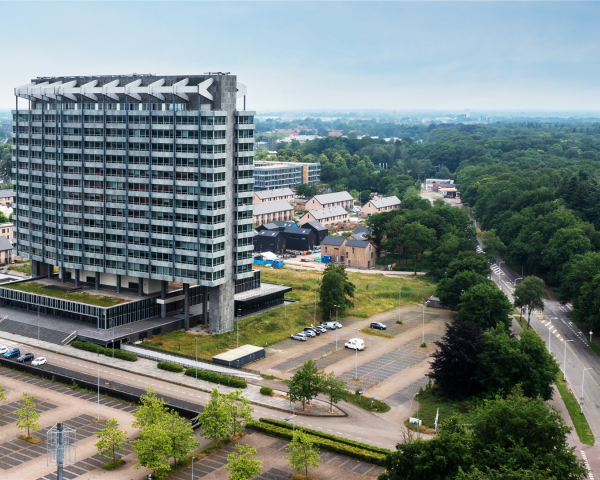 Luchtfoto van het VB-terrein in Eindhoven met een markant hoogbouwgebouw, omliggende bebouwing, groenvoorzieningen en de locatie waar de ontwikkeling van nieuwe appartementen plaatsvindt.